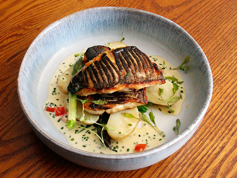 Pan-fried sea bass fillets, mixed greens and Jersey Royals, with a white wine cream